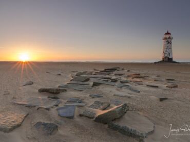 The sun setting on Talacre Beach with Talacre Lighthouse in the middle distance